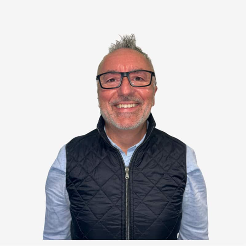 Portrait Homme Souriant Lunettes Gilet Noir Homme souriant d'âge moyen, portant des lunettes à monture noire et un gilet matelassé noir sur une chemise bleue, avec une coiffure courte et ébouriffée.