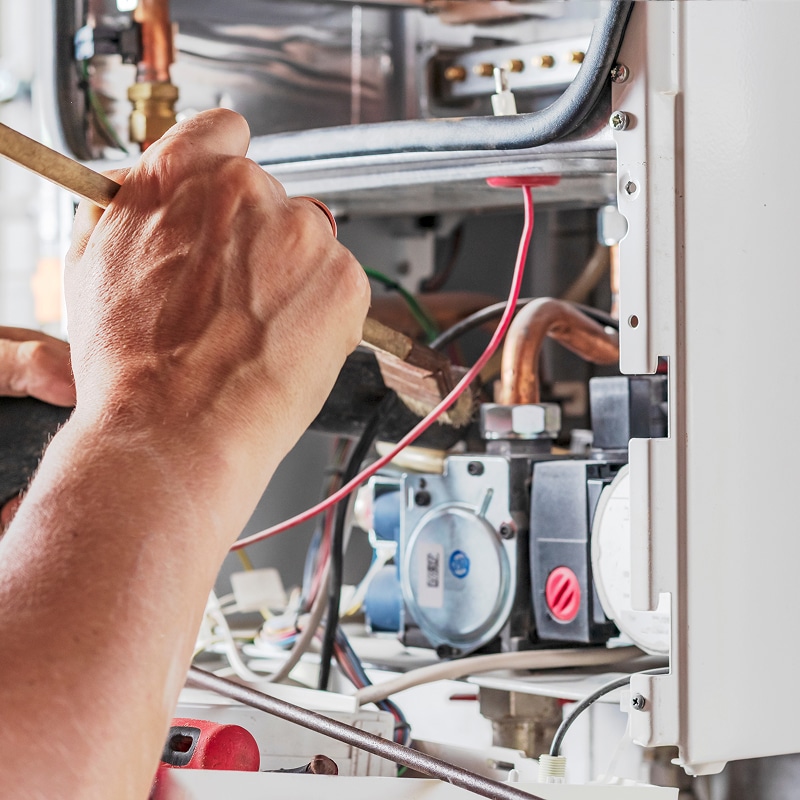Réparation chaudière : technicien vérifiant le bloc gaz Main d'un technicien utilisant un outil en bois pour travailler sur les composants internes complexes d'une chaudière ou d'un chauffe-eau mural.